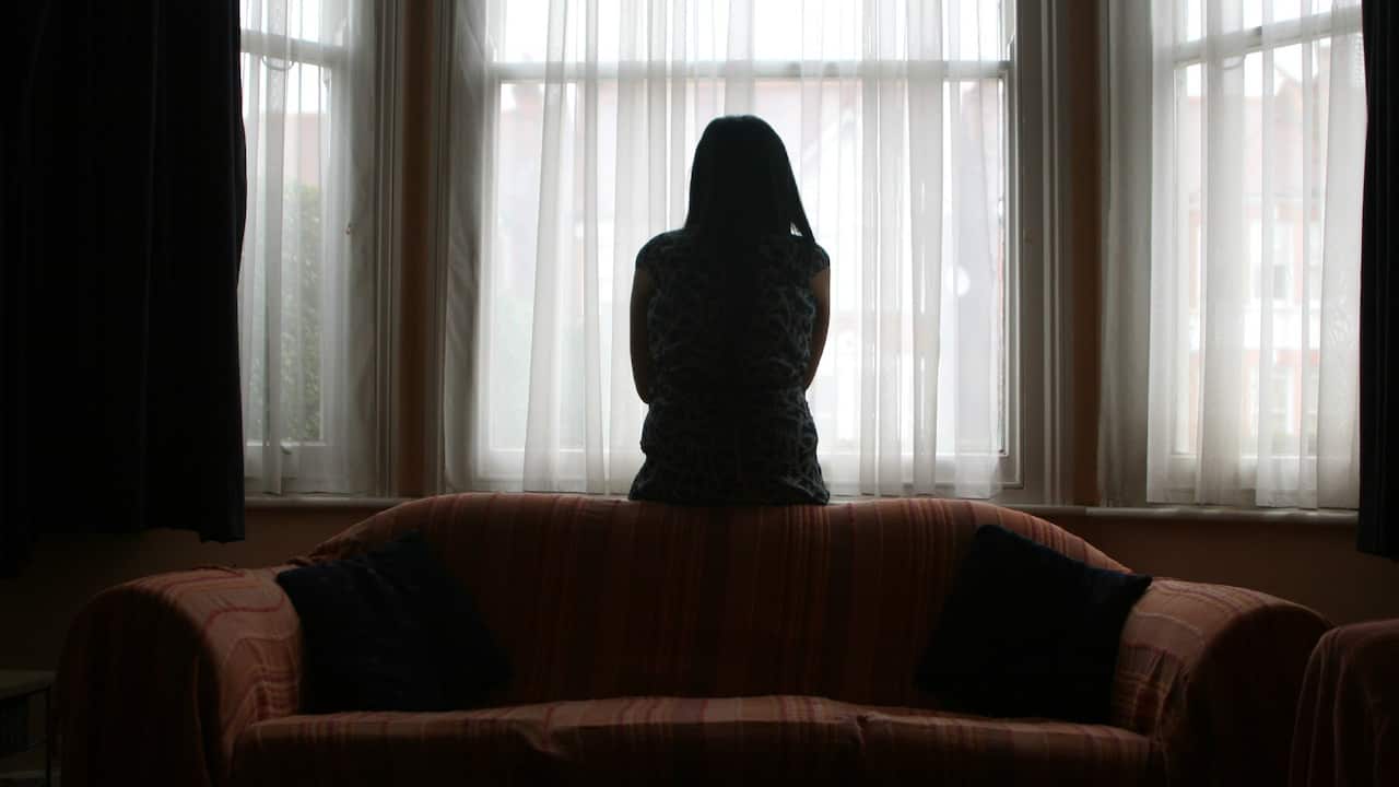 A silhouette of a woman standing behind a curtain in a living room.