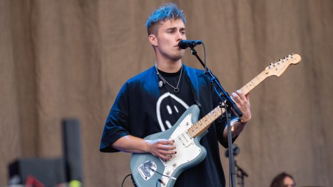 Musician and actor Sam Fender is holding a guitar and singing into a microphone.